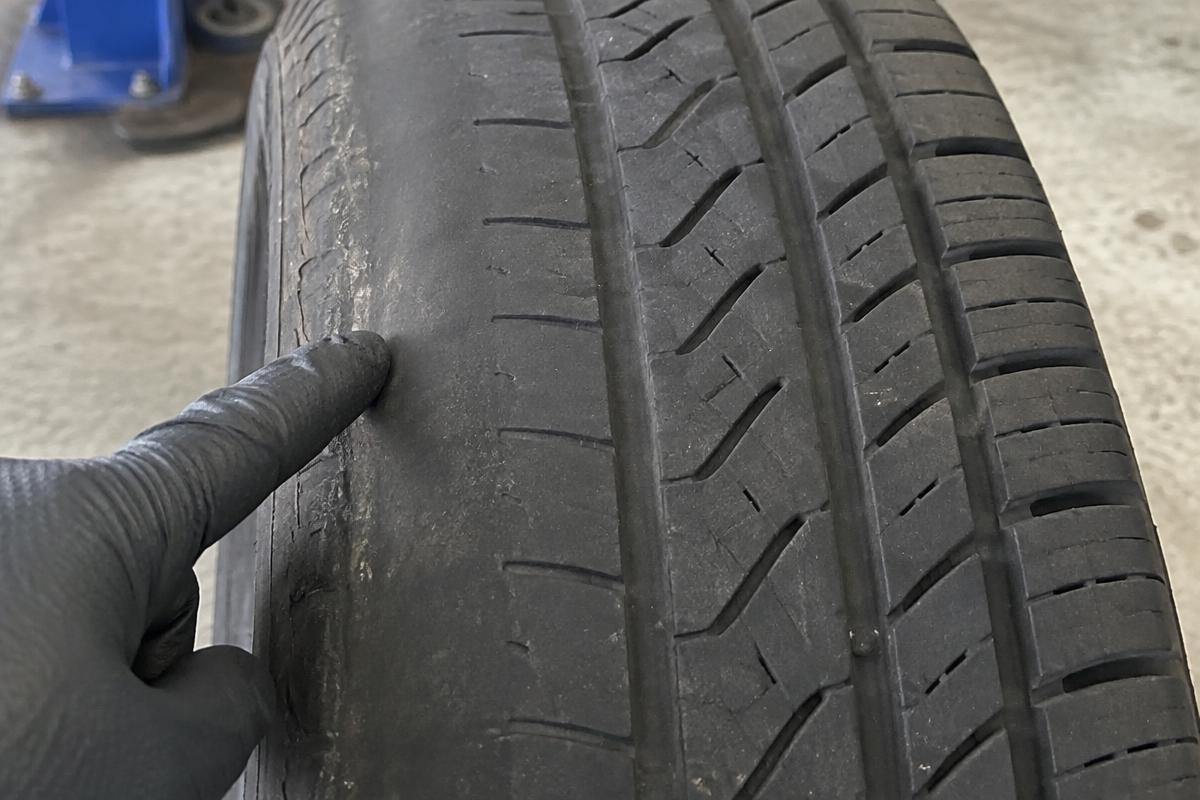 Close-up of a car tyre worn smooth along the inside edge, with a gloved finger pointing at the wear