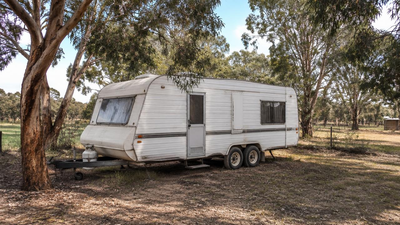 Caravan parked under gum trees on a rural property, the kind of vehicle whose tyres age before they wear out