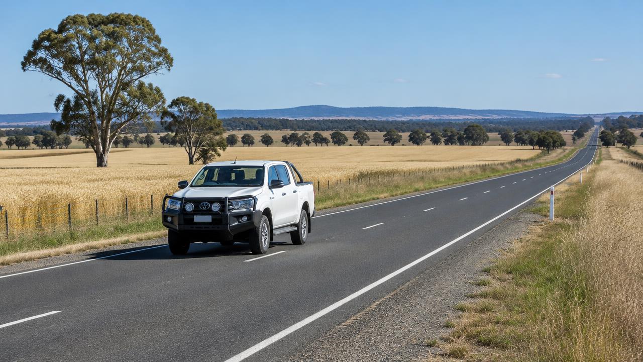 White 4WD ute driving along a straight country highway past wheat paddocks in regional NSW